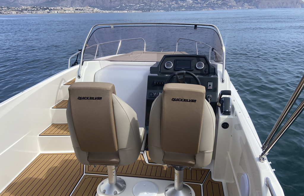 Quicksilver 675 Sundeck vista desde popa mostrando escaleras a solárium, sillones ergonómicos, puesto de mando y acceso a cabina con dos camas