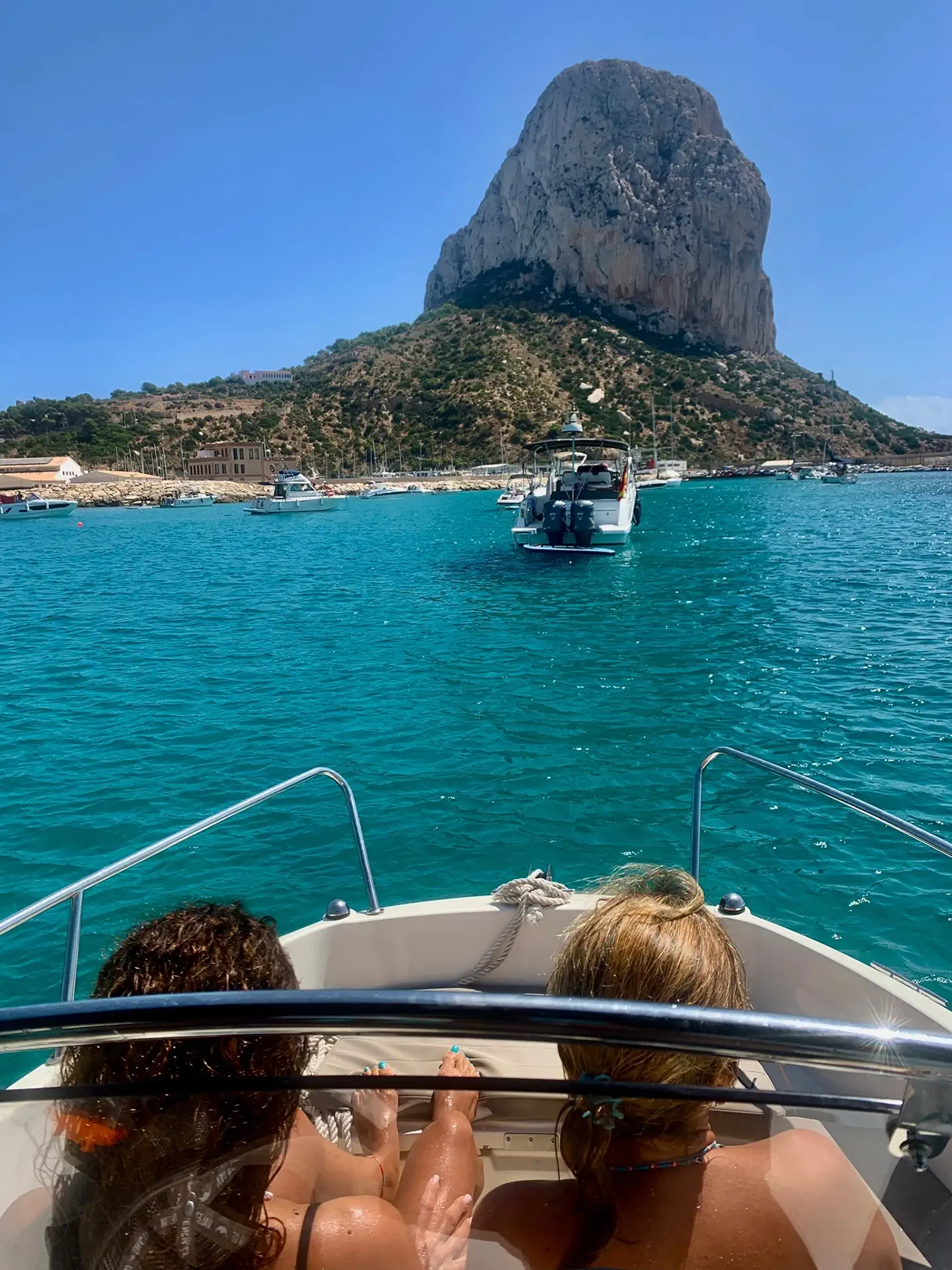 Two women on anchored Quicksilver 605 watching boats near Calpe harbor with the Peñón de Ifach in the background
