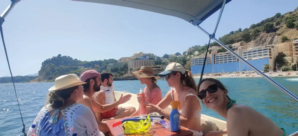 Group of friends sitting around a table on a boat talking with Marina Greenwich harbour visible in the background in Altea.