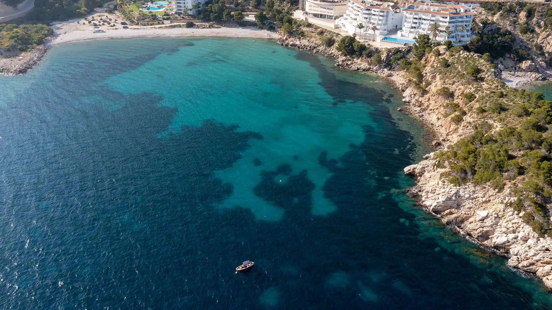 Drone aerial view of boat moored to buoy above visible Posidonia seagrass through crystal-clear water at Mascarat beach, Altea