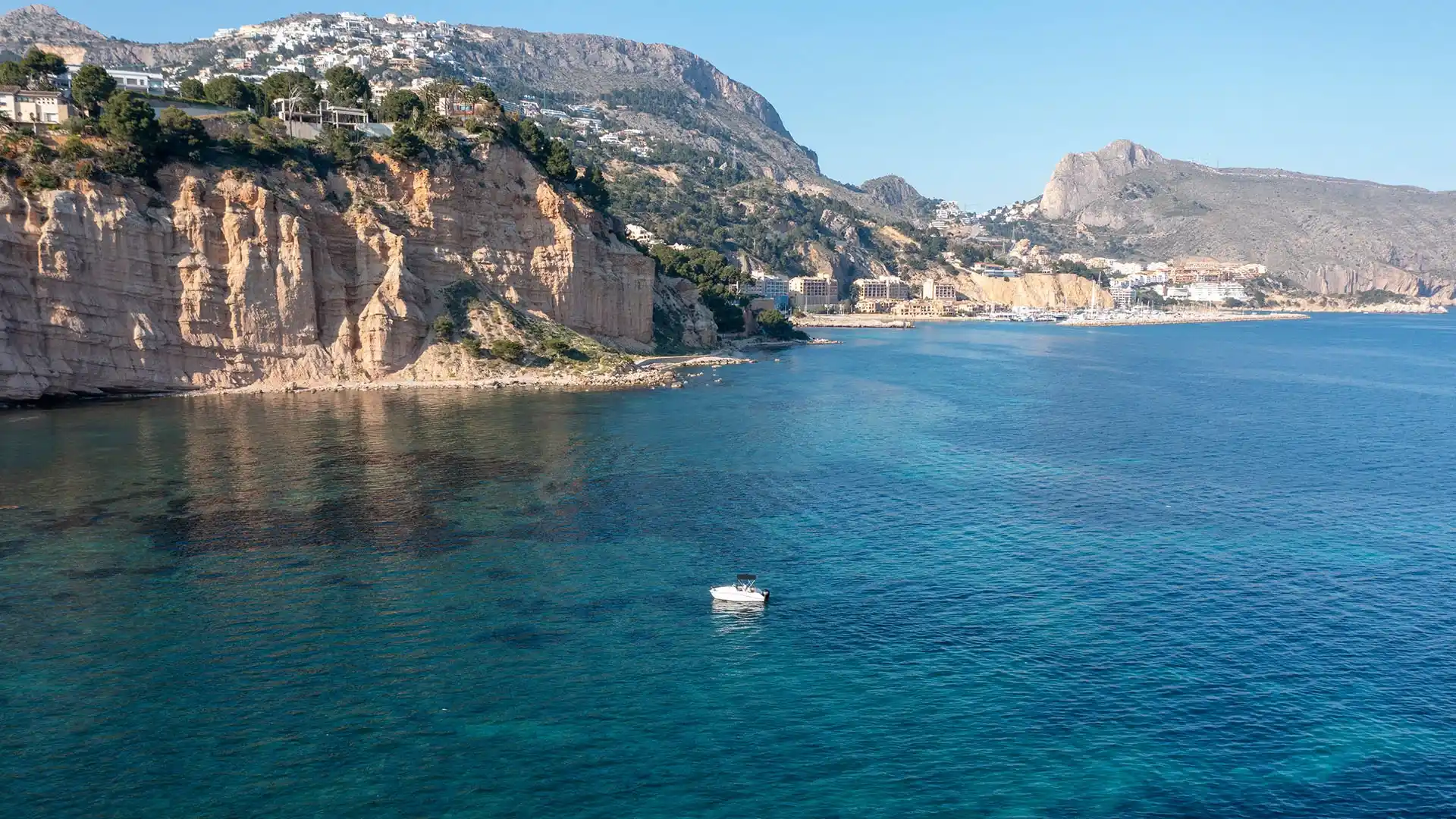 Vista aérea de barco fondeado en aguas turquesas junto a los acantilados de Mascarat con la costa de Calpe al fondo
