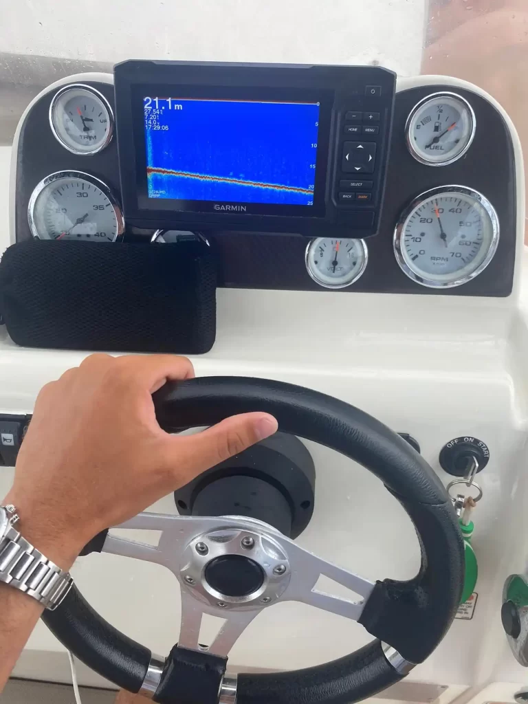 Helm station of a Quicksilver 505 Open with Garmin GPS screen on and a man's hand on the wheel while navigating on the Costa Blanca.