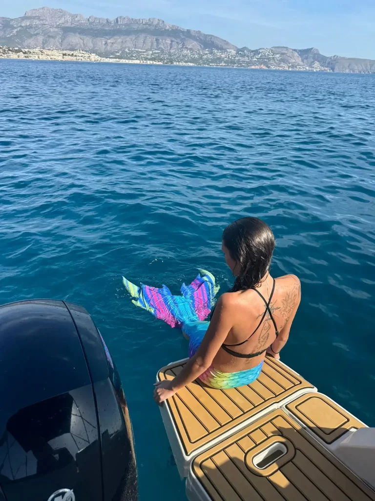 Woman with a mermaid tail sitting on the stern of a Quicksilver boat looking at the sea in Altea on the Costa Blanca.